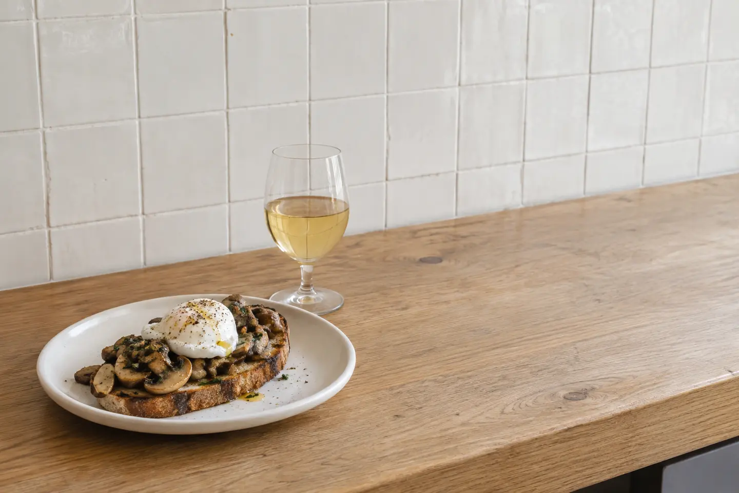 One mushroom toast and one glass of white wine on an ordinary fictional bistro counter.